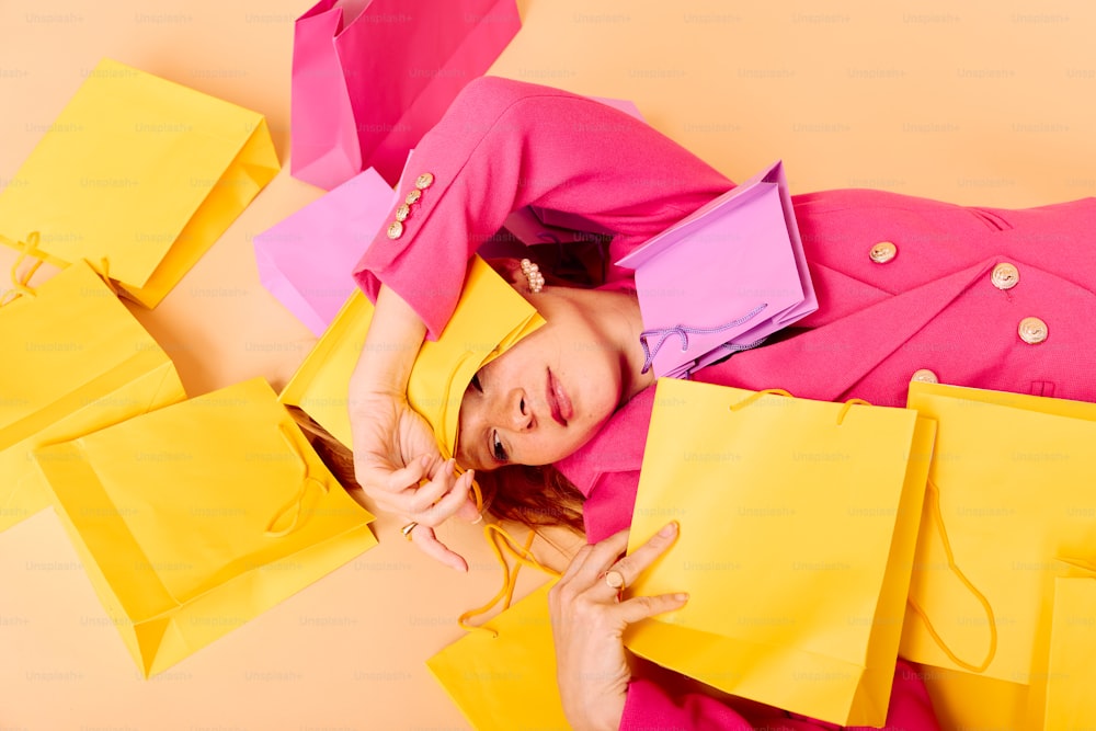 a woman laying on top of a pile of yellow and pink bags