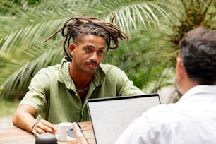 a man with dreadlocks sitting at a table with a laptop