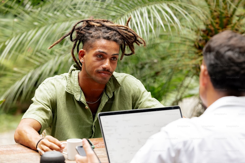 a man with dreadlocks sitting at a table with a laptop