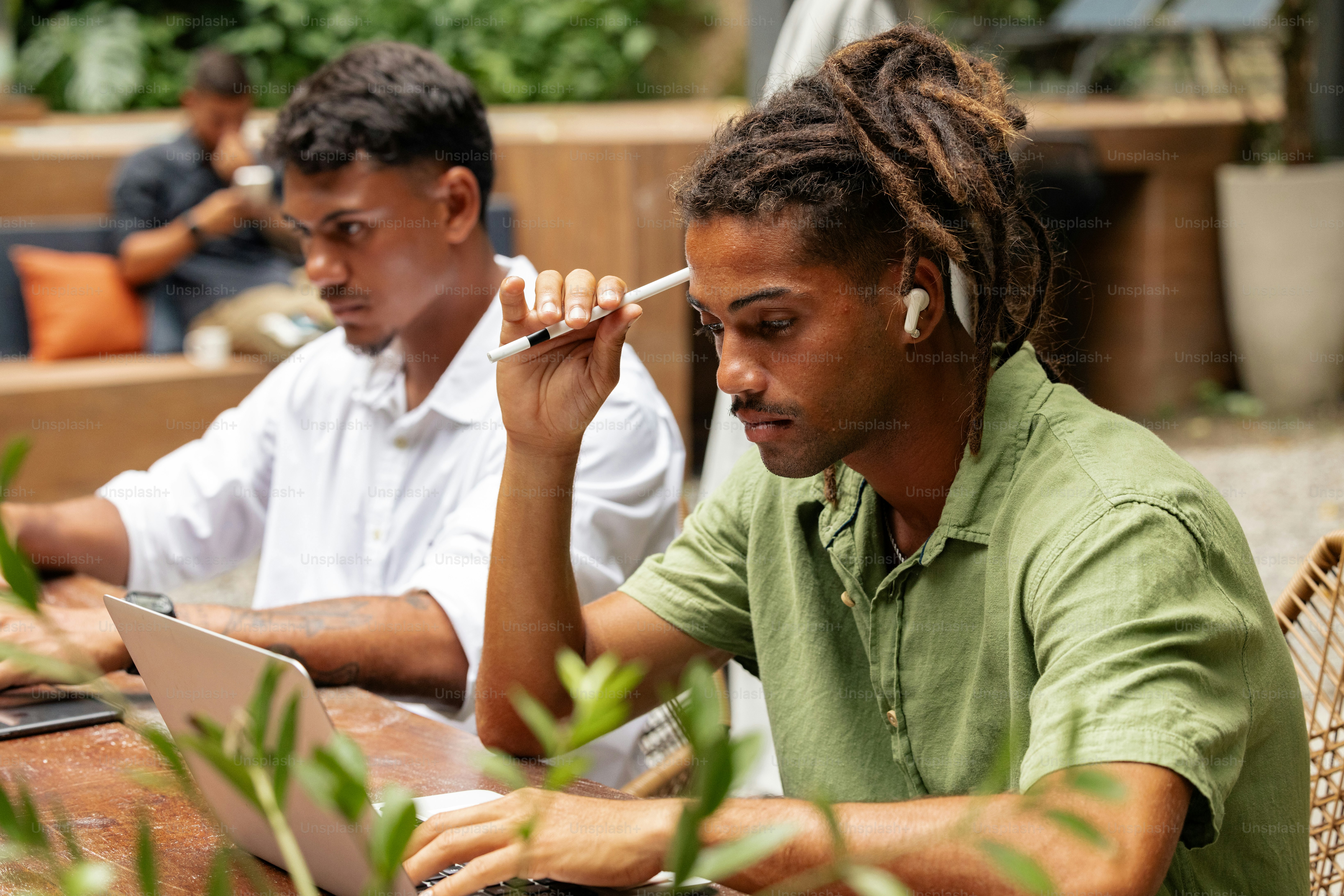 Ein Mann sitzt mit einem Laptop und einer Zigarette im Mund an einem Tisch