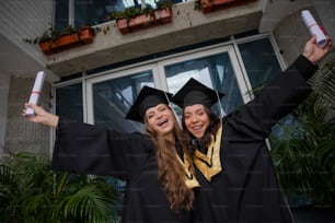 Dos mujeres con togas de graduación sosteniendo sus diplomas