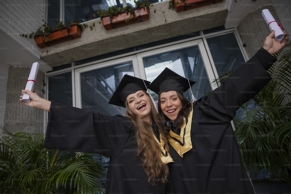 two women in graduation gowns holding up their diplomas