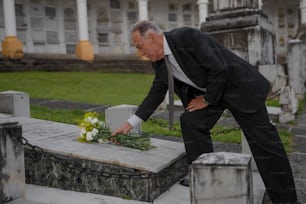 a man in a suit placing flowers on a grave