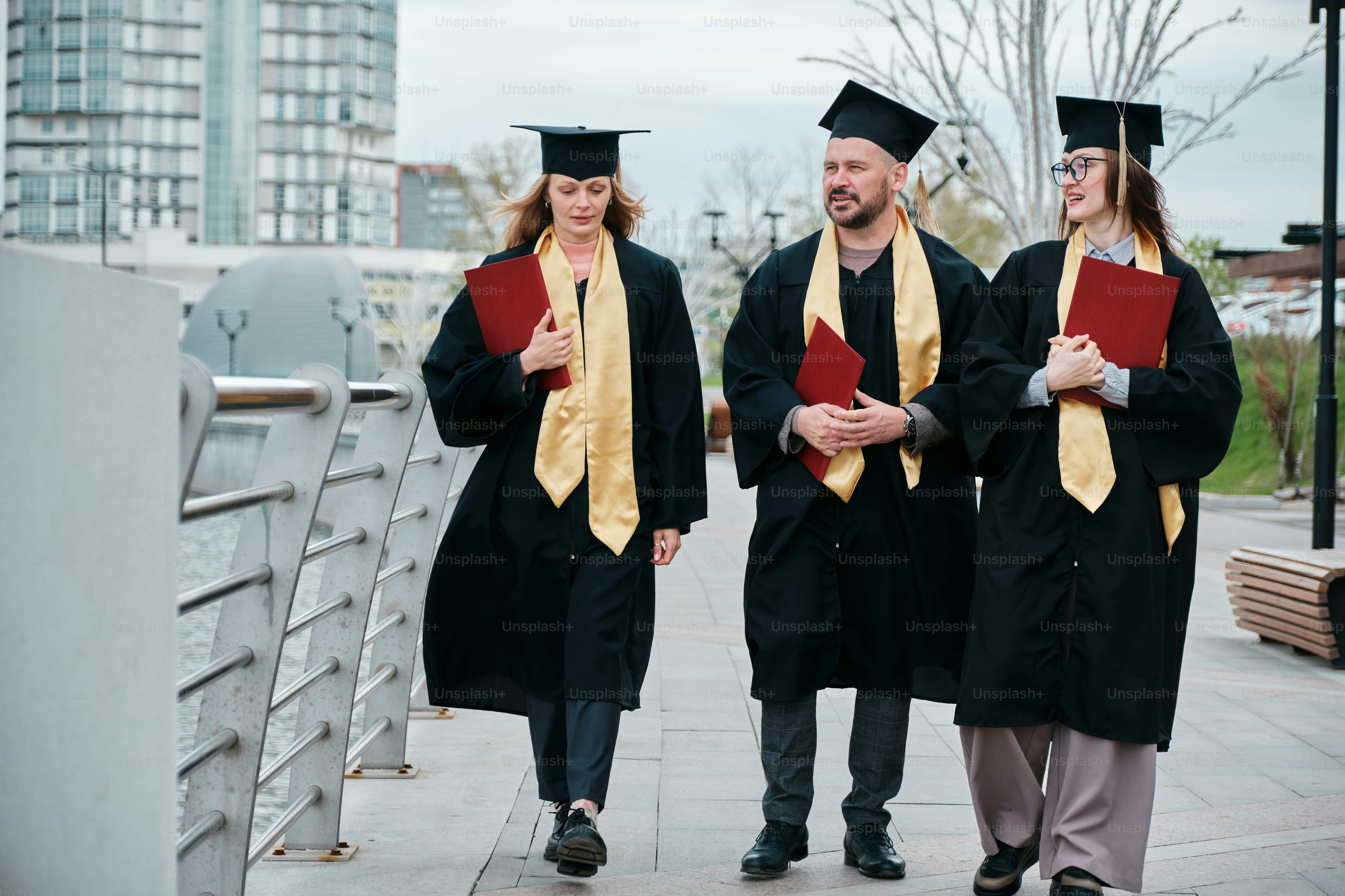 a group of three graduates walking across a bridge