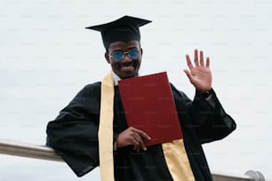 Un hombre con una toga de graduación sosteniendo un libro rojo
