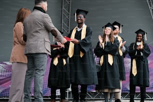 Un grupo de personas con togas de graduación de pie frente a un escenario
