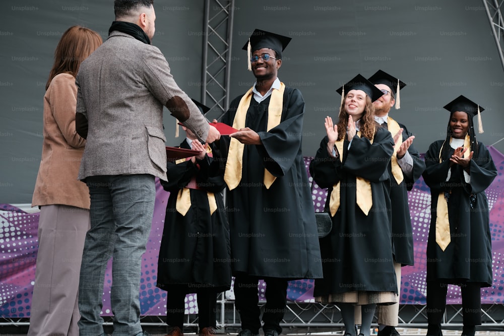 a group of people in graduation gowns standing in front of a stage