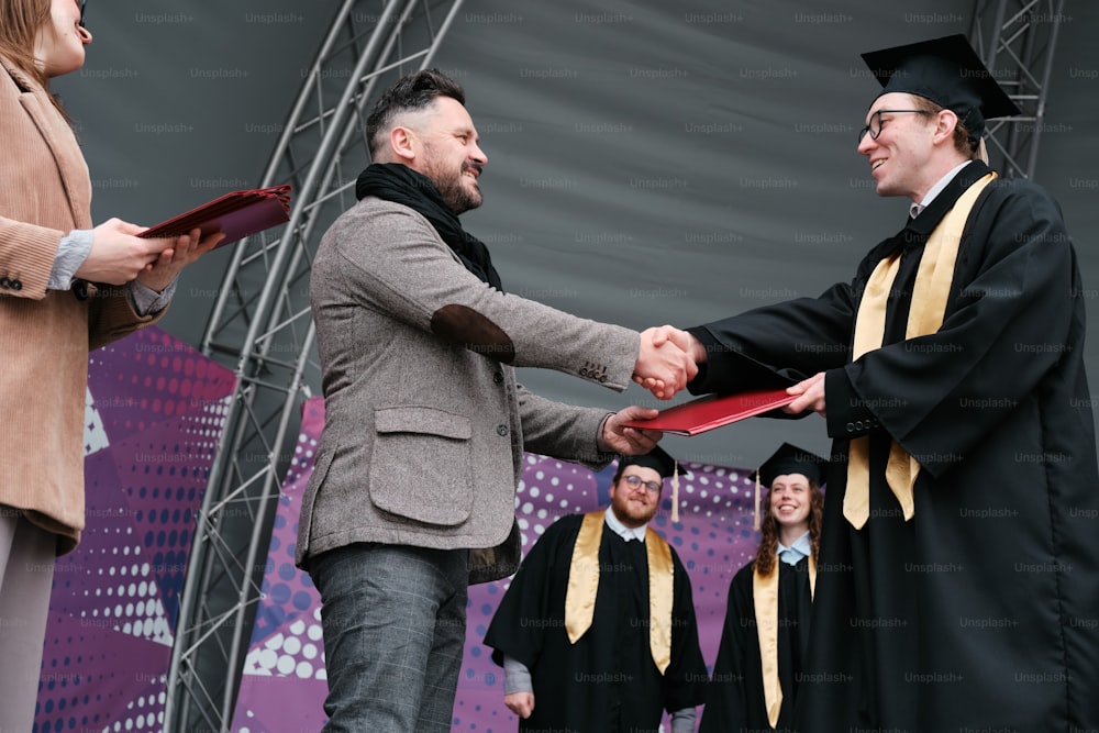 a man in a graduation gown shaking another mans hand