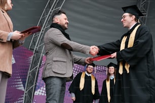 a man in a graduation gown shaking another mans hand