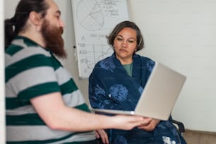 a woman holding a laptop in front of a man