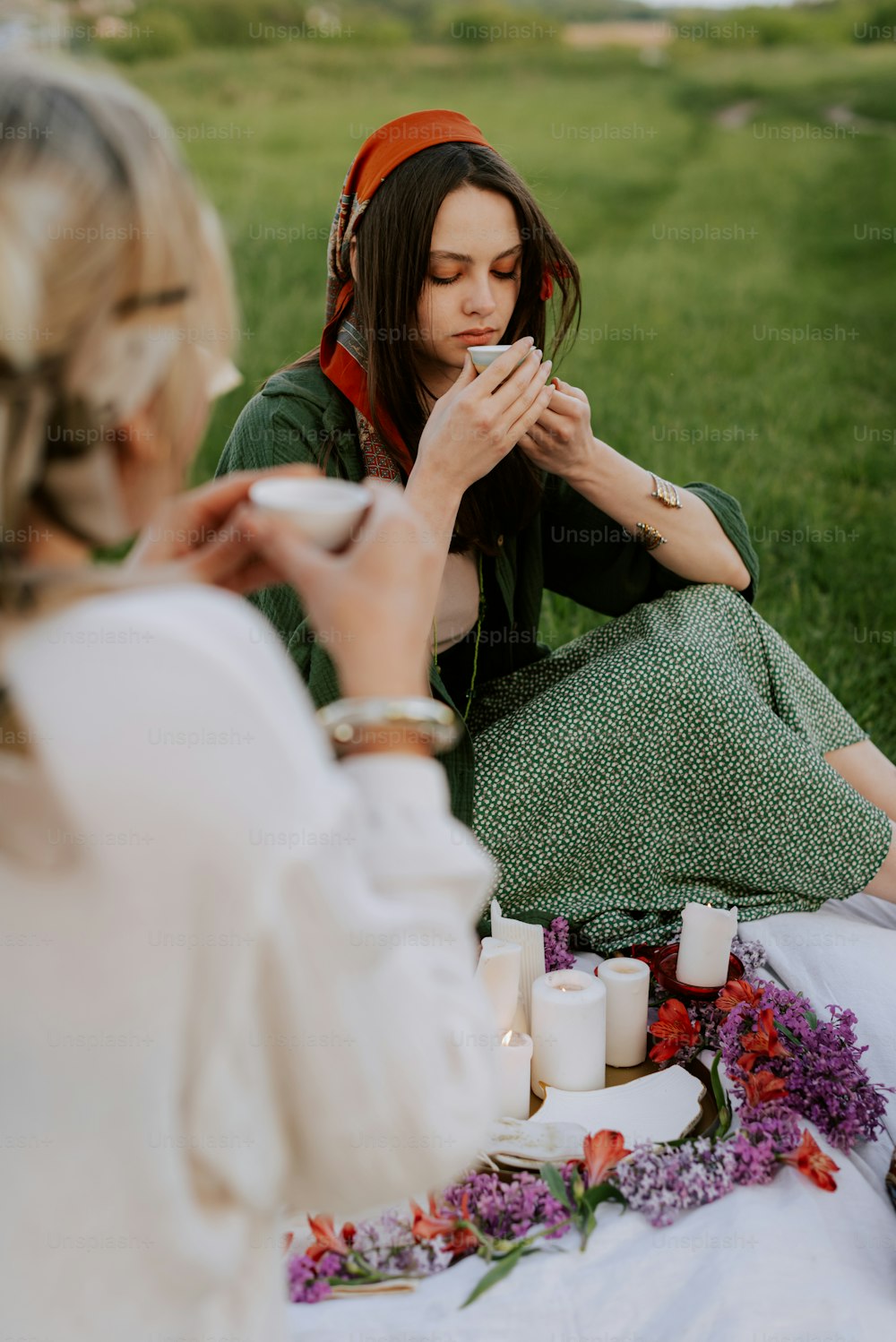 a couple of women sitting on top of a lush green field