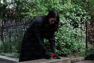 a woman with long hair and sunglasses placing a flower on a wall