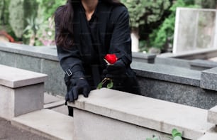 una mujer vestida de negro sosteniendo una rosa roja