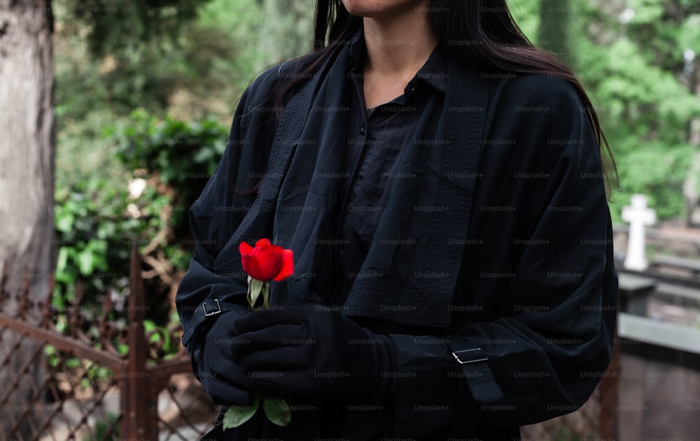 eine Frau in einer schwarzen Jacke, die eine rote Rose in der Hand hält