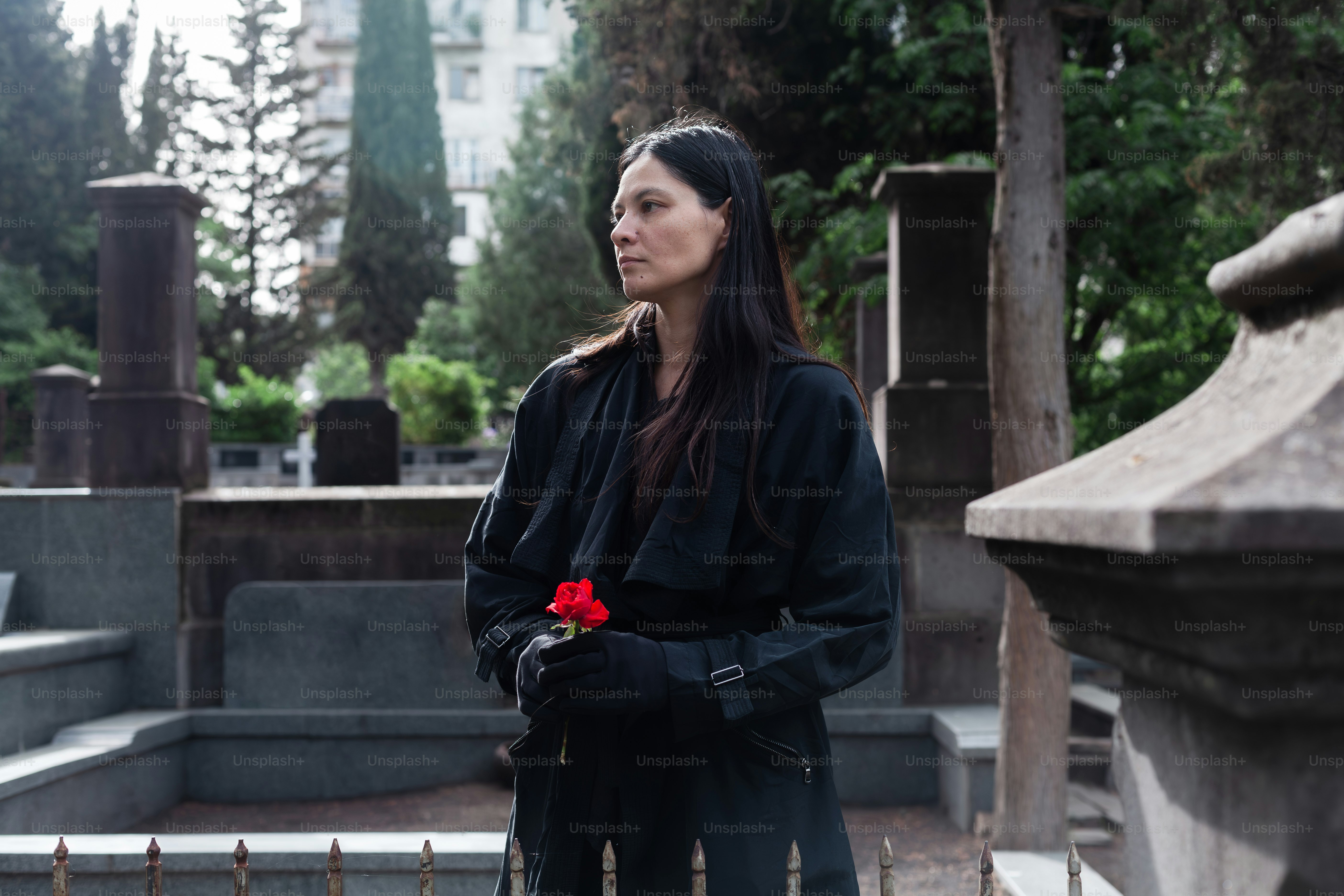 a woman standing in a cemetery with a rose in her hand