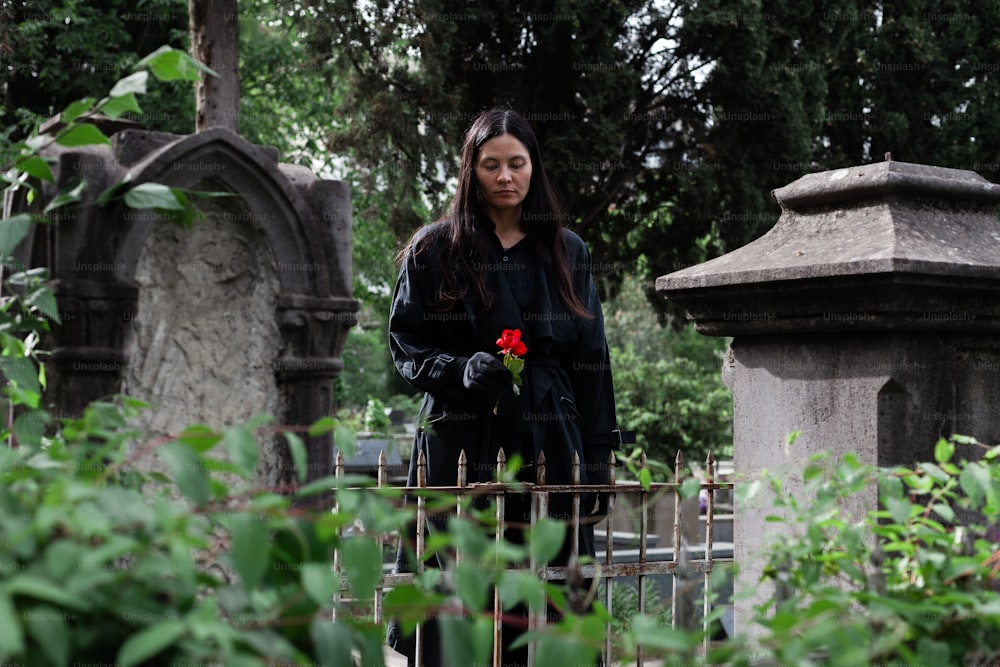 a woman standing in a cemetery with a rose in her hand