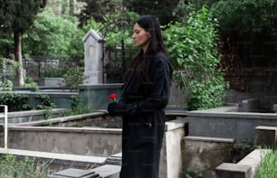 a woman standing in a cemetery with a rose in her hand