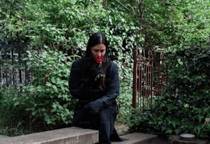 una mujer sentada en un banco de piedra con una flor en la boca