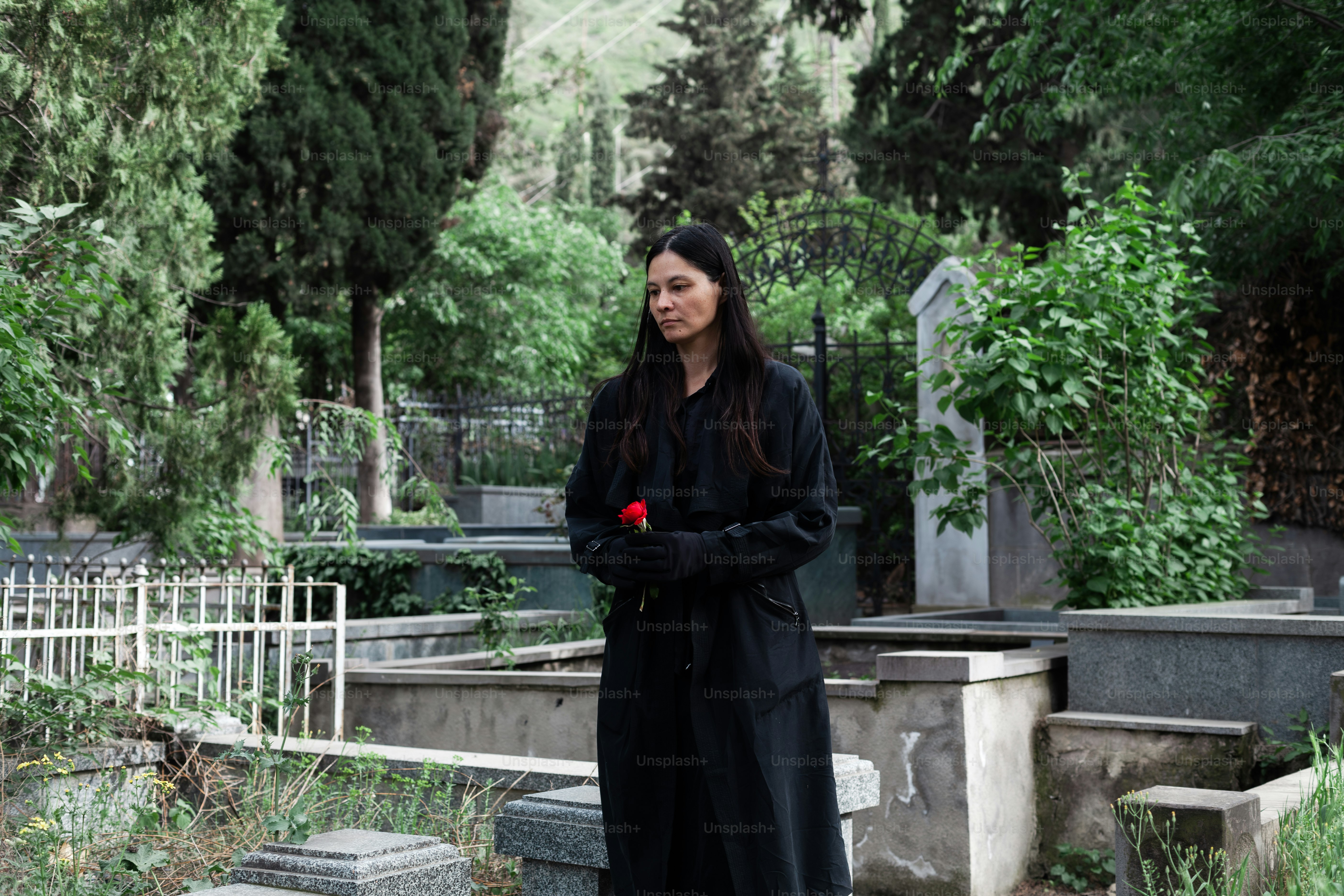 a woman in a long black coat standing in a cemetery