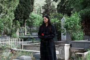 a woman in a long black coat standing in a cemetery