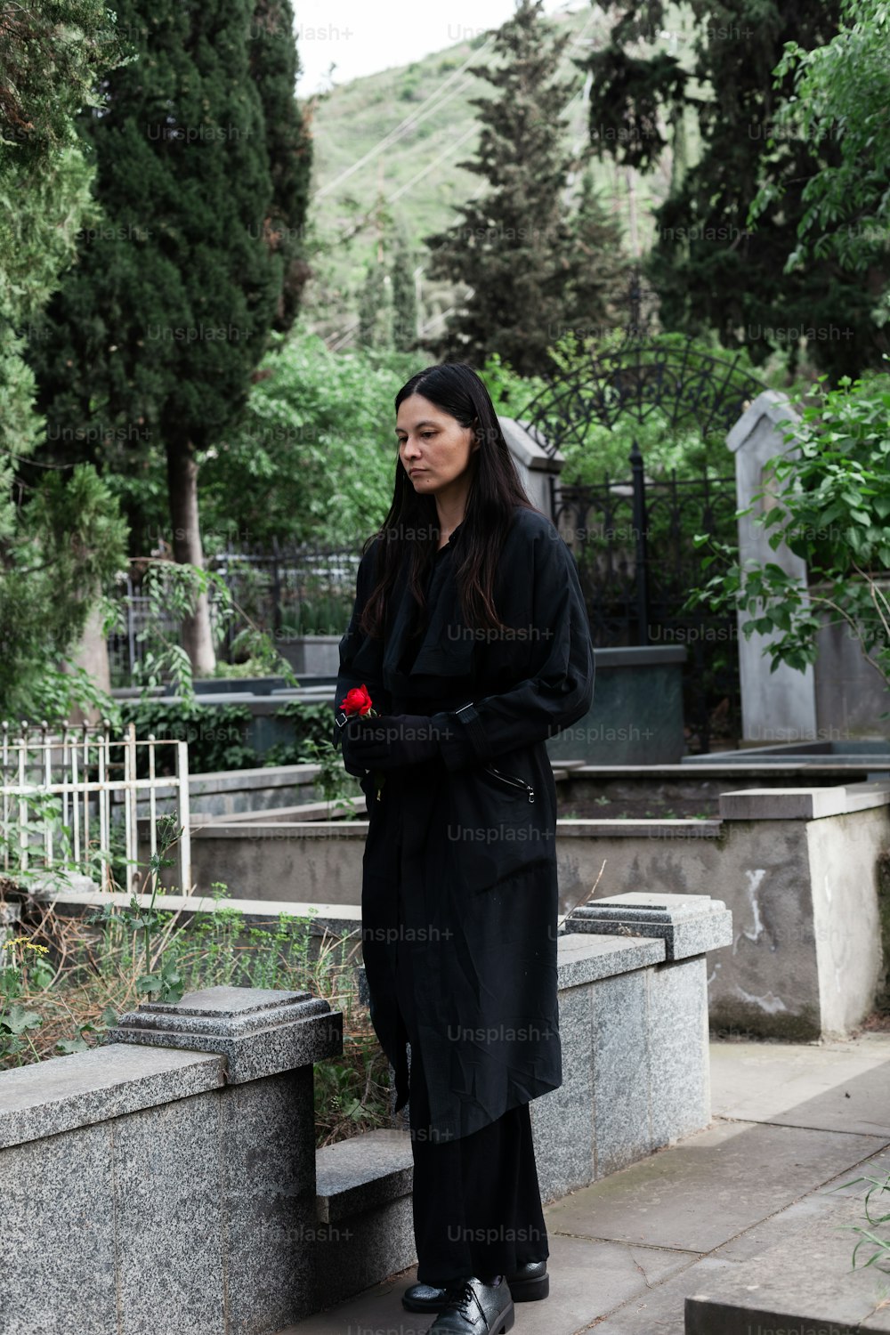 a woman in a long black coat standing on a stone bench