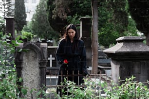 a woman standing in a cemetery with a rose in her hand