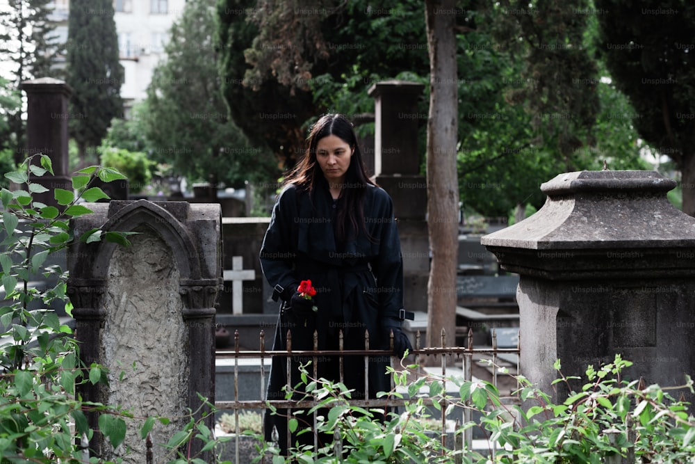 uma mulher em pé em um cemitério com uma rosa na mão