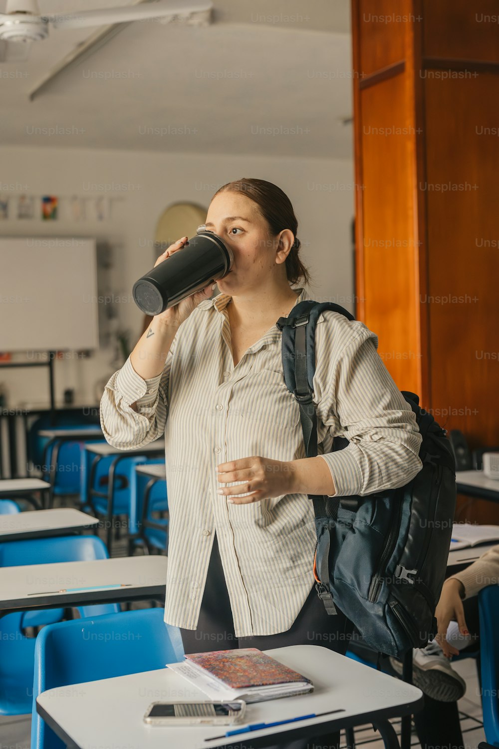 a woman standing in a classroom drinking from a cup