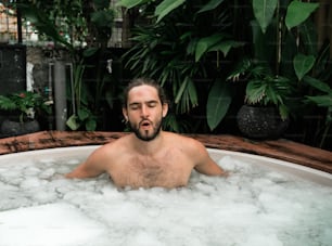 Un hombre en una bañera de hidromasaje con plantas en el fondo