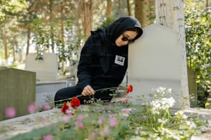 검은 후드티를 입은 여자가 무덤에 앉아 있다