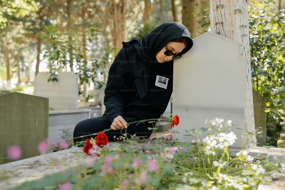 uma mulher com capuz preto sentada em um túmulo