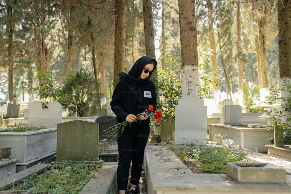 a woman in a black hoodie holding flowers in a cemetery