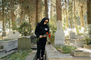 a woman in a black hoodie holding flowers in a cemetery
