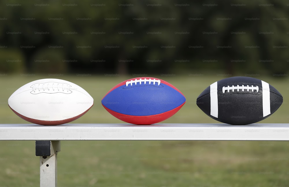 three different types of footballs sitting on a bench