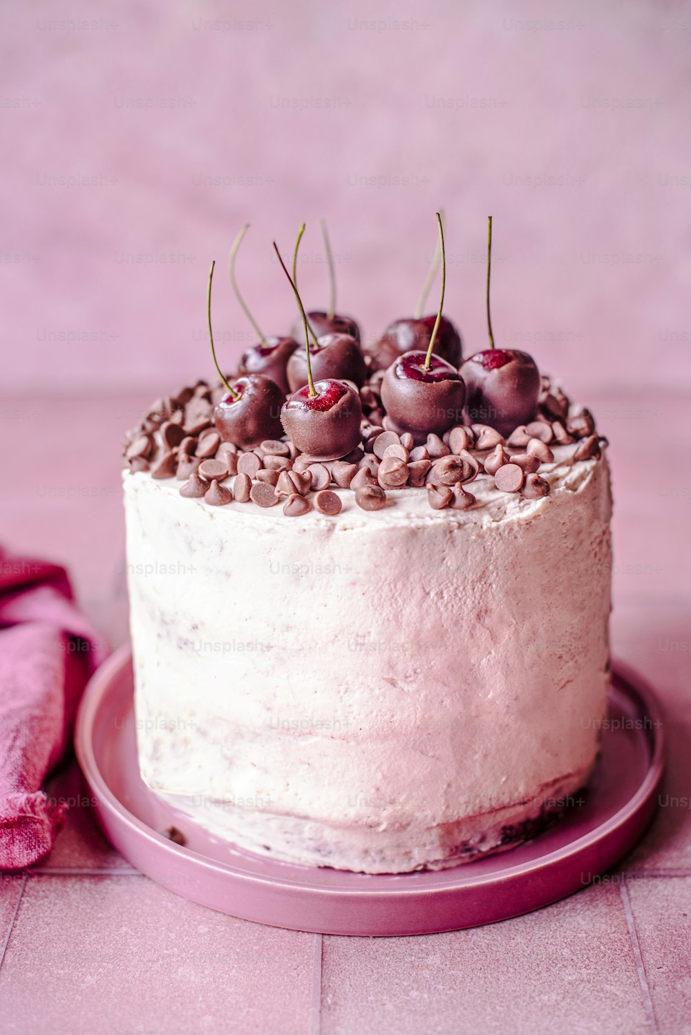 a cake with white frosting and cherries on a pink plate