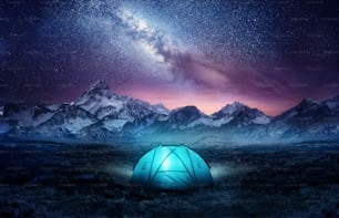 Acampar nas montanhas sob as estrelas. Uma tenda erguida e brilhando sob a Via Láctea. Composição de fotos.