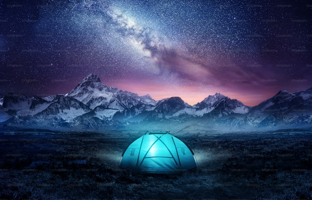 Camping in the mountains under the stars. A tent pitched up and glowing under the milky way. Photo composite.