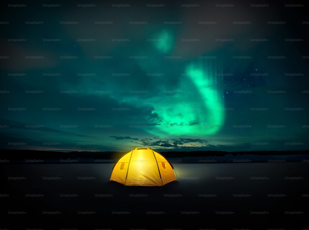 Out in the wilderness The Norther lights ( Aurora Borealis) dances across the night sky in Sweden, above the glowing lights from the camping tent. Photo Composite.