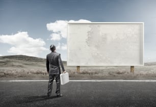 A business man standing and staring at a blank billboard advertisement.