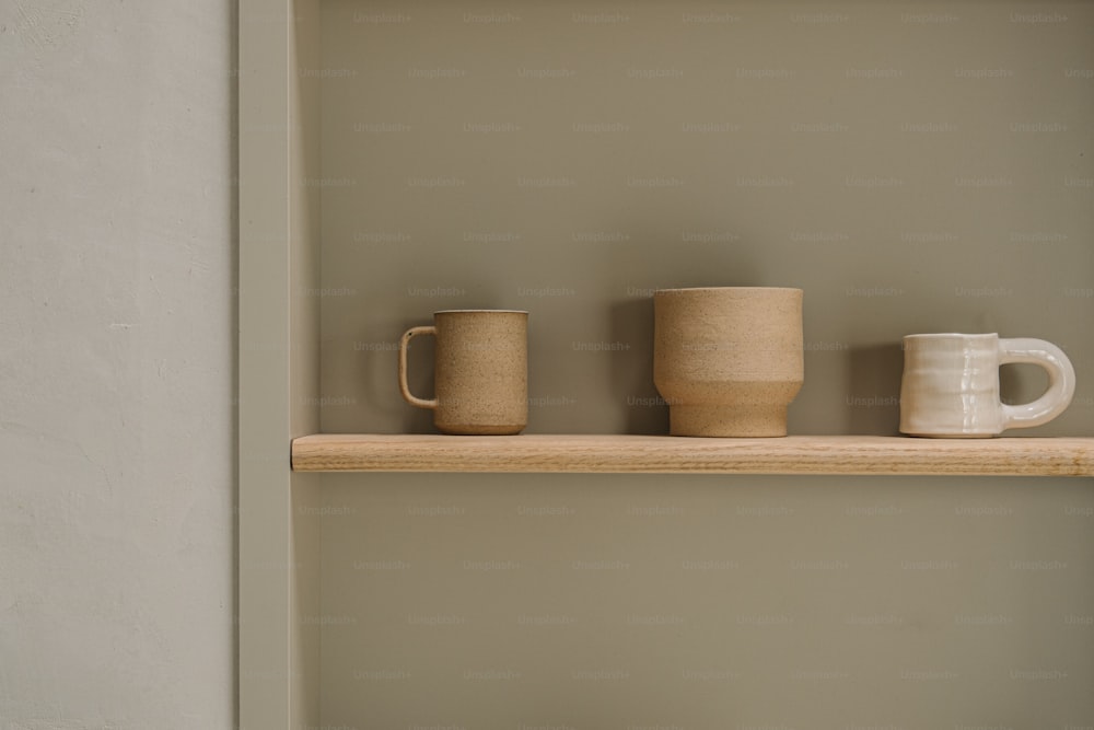 três canecas de café estão sentadas em uma prateleira