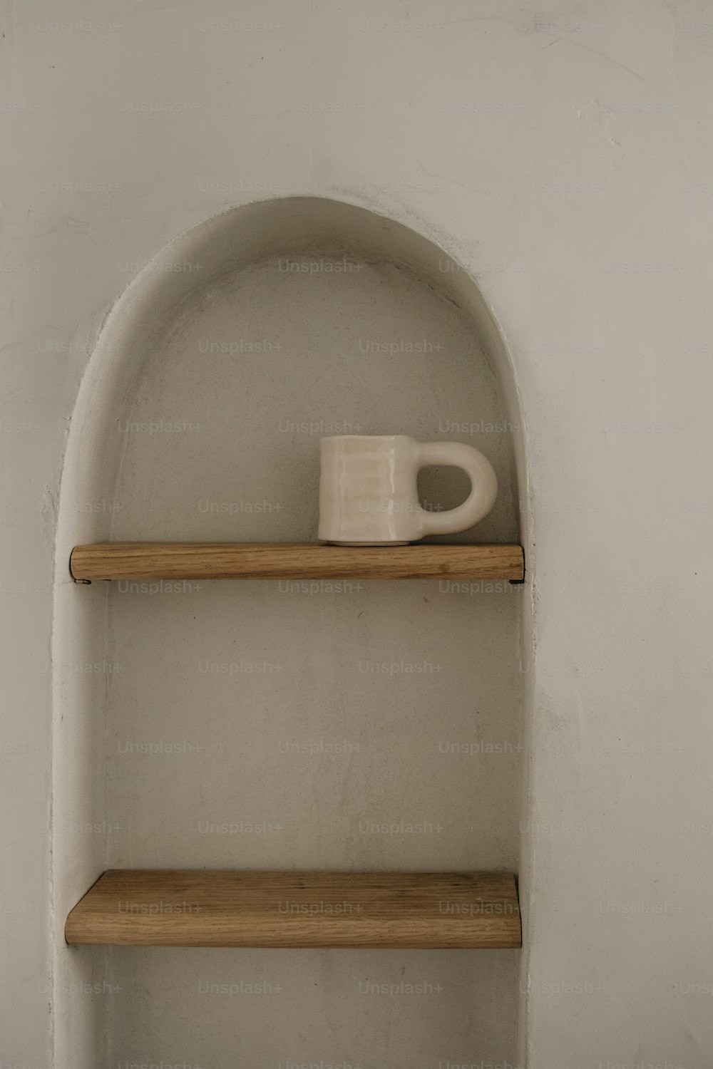 uma caneca branca sentada em cima de uma prateleira de madeira