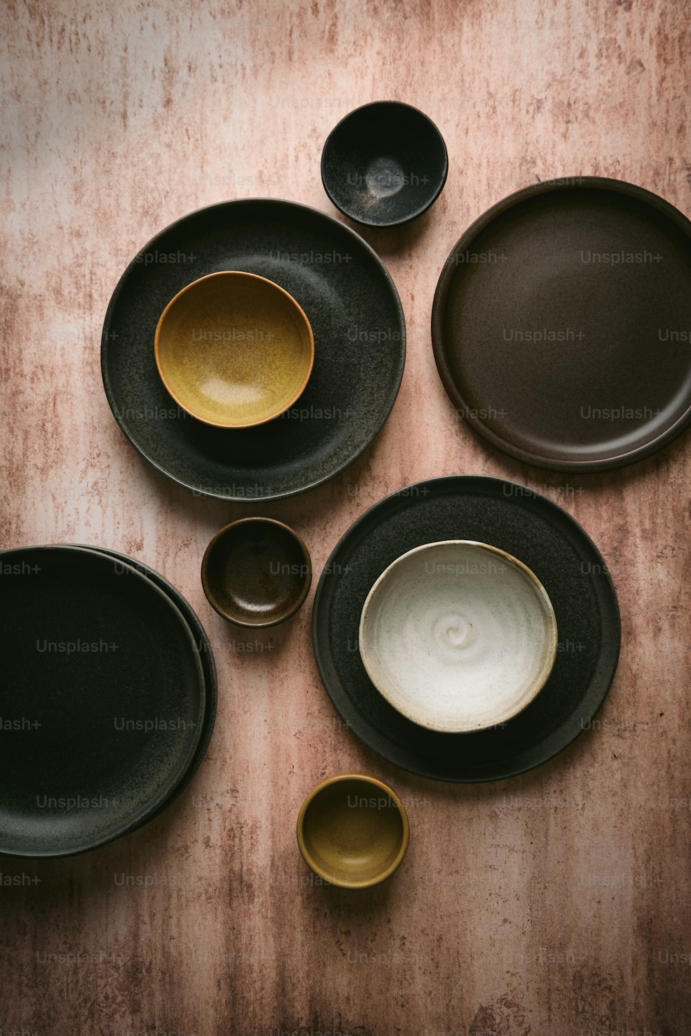 a wooden table topped with black plates and bowls