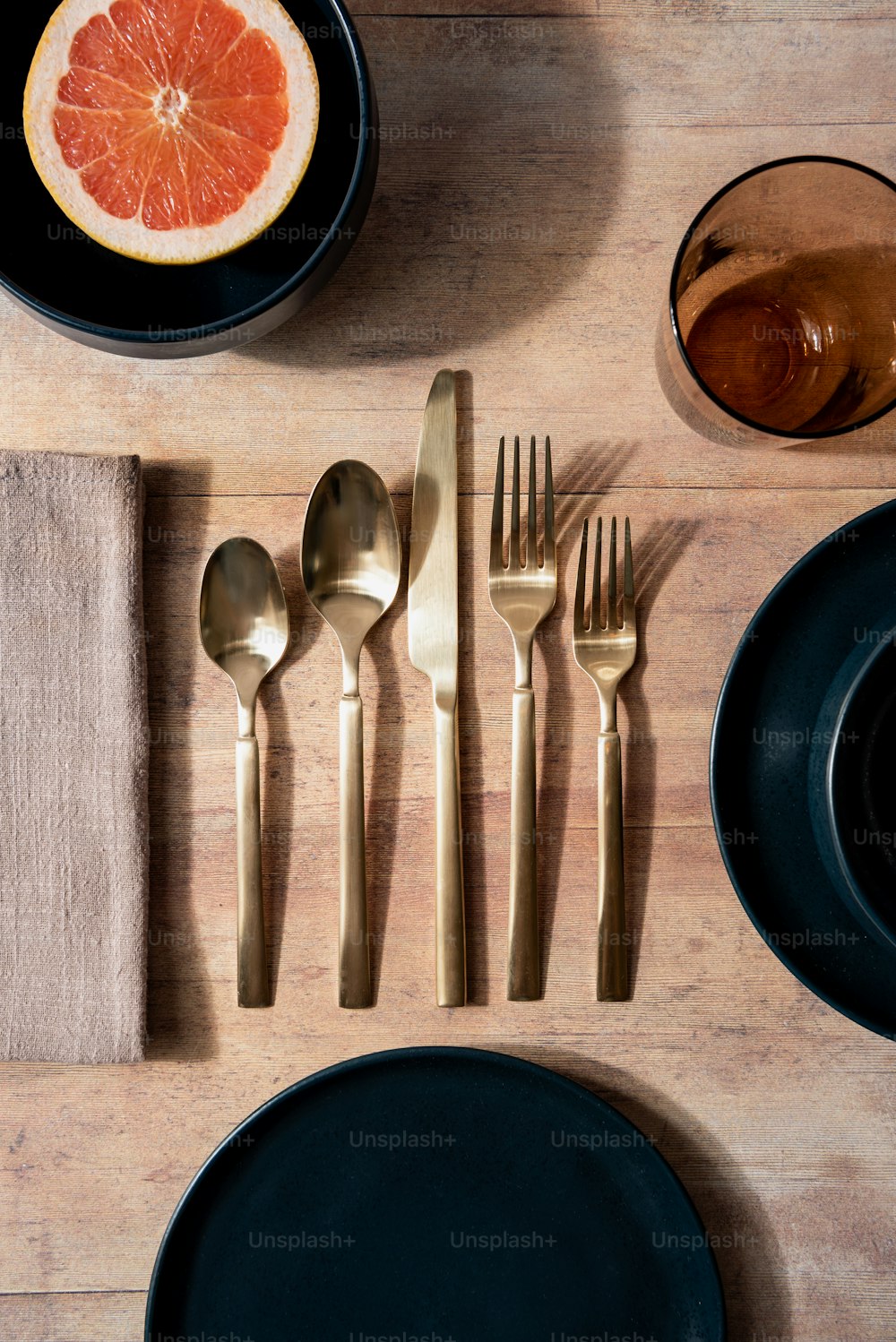 a wooden table topped with black plates and silverware