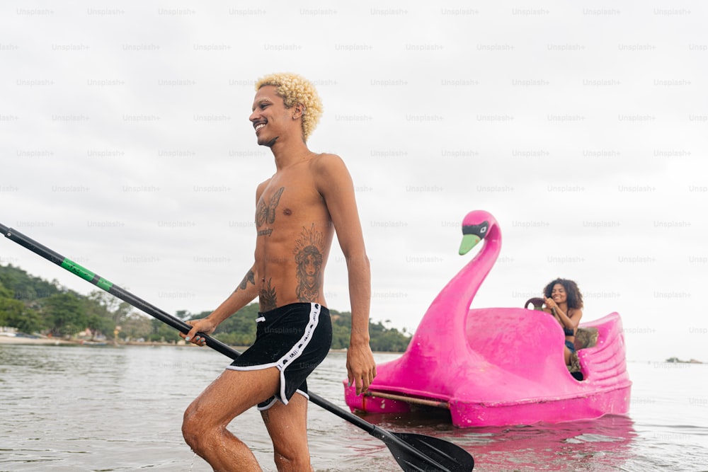 a man riding a paddle board next to a pink flamingo boat