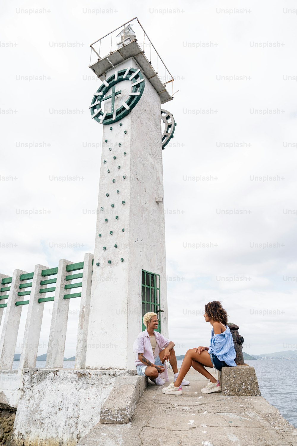 a man and a woman sitting on a pier next to a lighthouse
