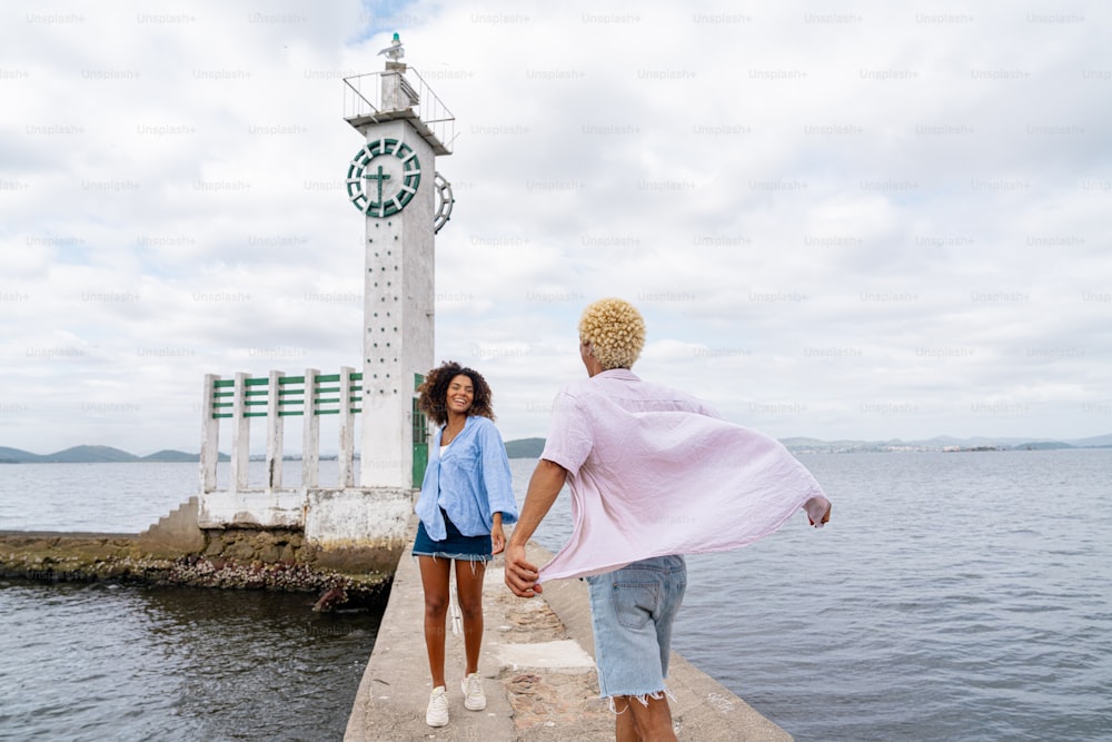 a man and a woman walking on a pier towards a clock tower