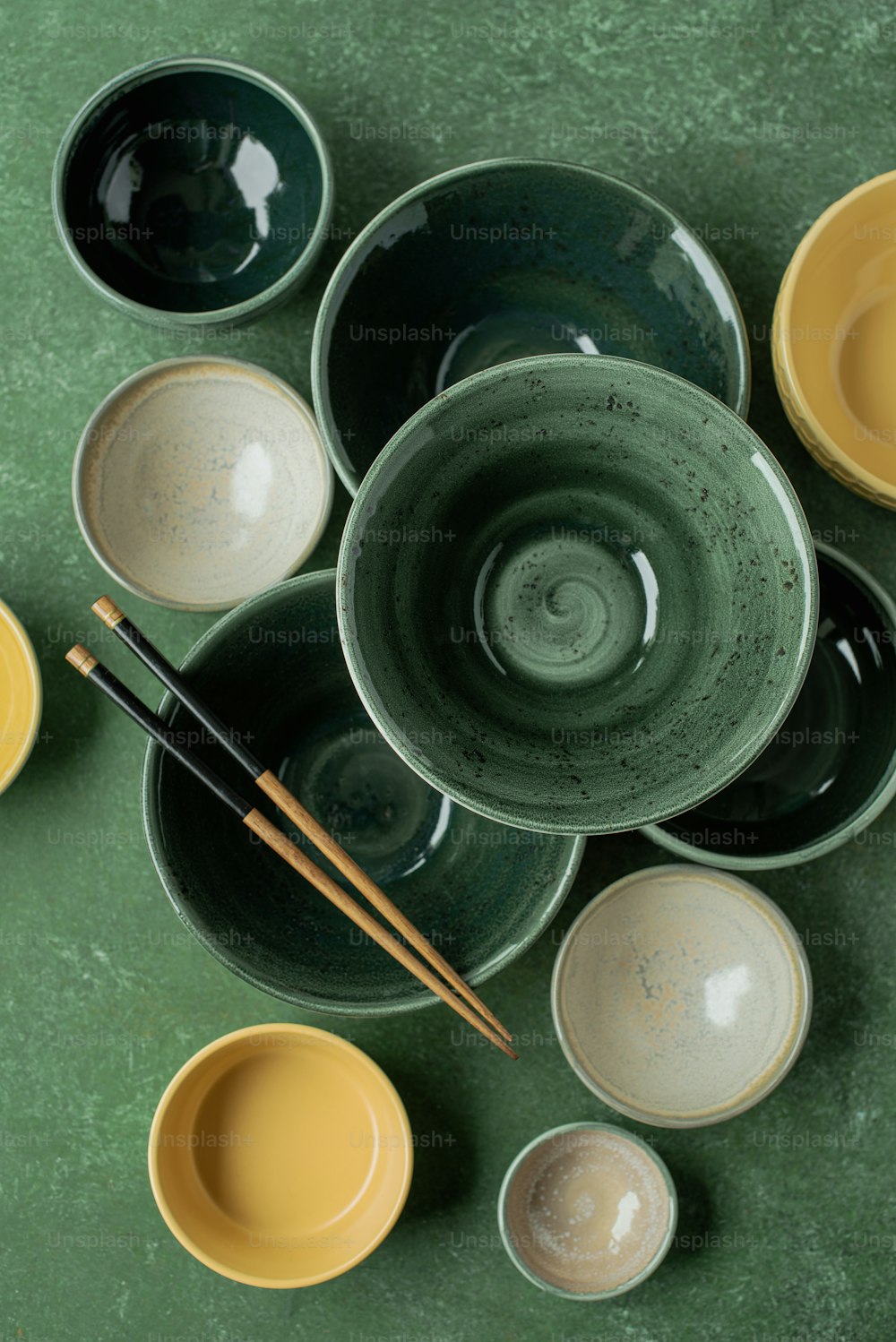 a green table topped with bowls and chopsticks