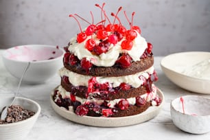 a triple layer cake with cherries and whipped cream