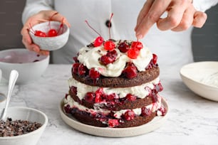 a person decorating a cake with cherries and whipped cream