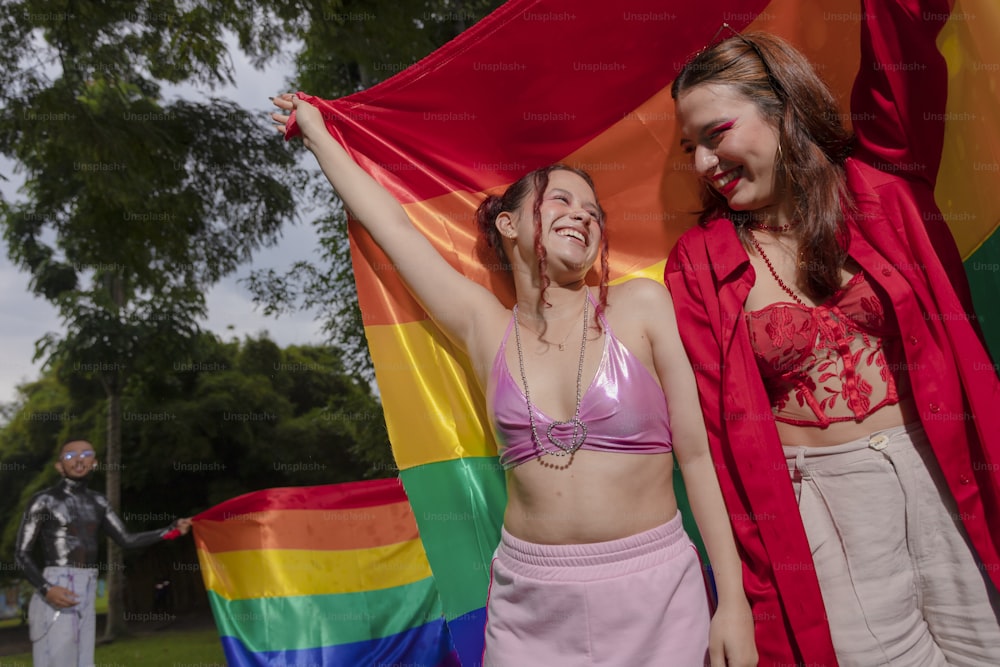 two women standing next to each other in front of a rainbow flag